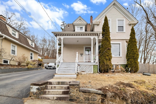 view of front facade featuring covered porch, a shingled roof, a chimney, and stairs