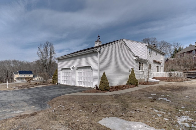 view of home's exterior featuring driveway, a garage, and a chimney