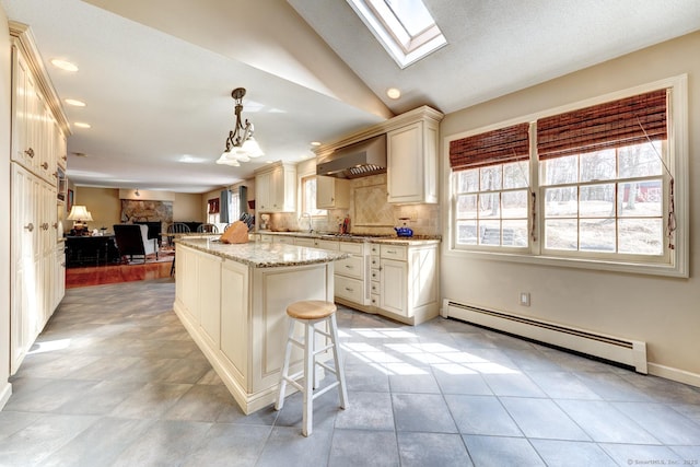 kitchen featuring light stone counters, baseboard heating, lofted ceiling with skylight, open floor plan, and ventilation hood