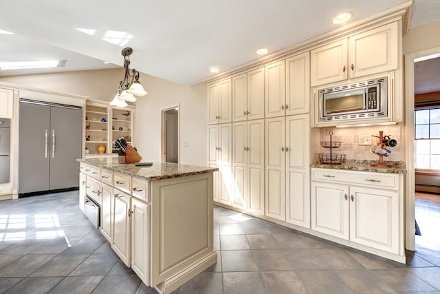 kitchen featuring a kitchen island, built in appliances, light stone countertops, vaulted ceiling, and cream cabinetry