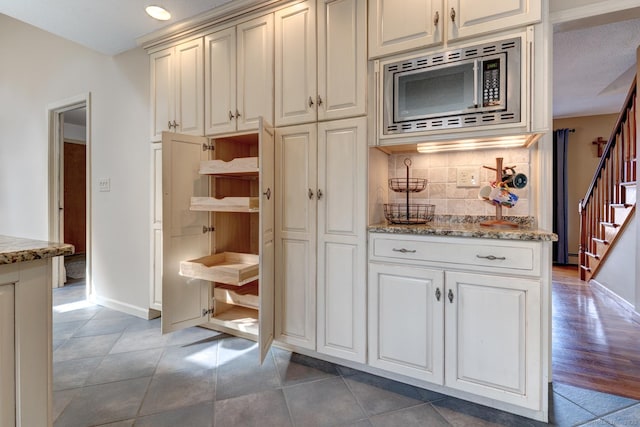 kitchen featuring light stone counters, stainless steel microwave, backsplash, and light tile patterned floors