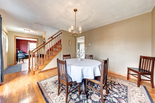 dining space featuring stairs, an inviting chandelier, baseboards, and light wood-style floors