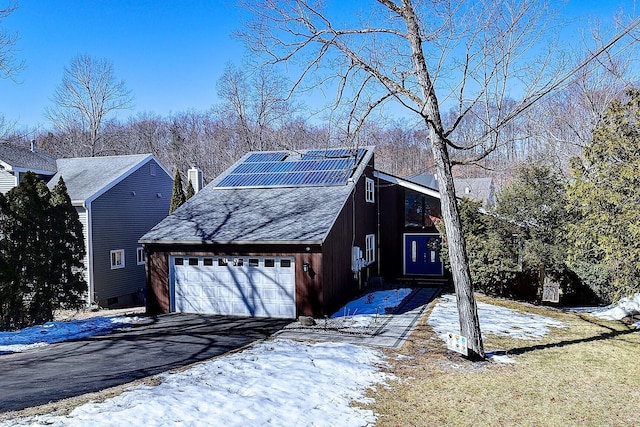 view of snowy exterior featuring a garage, a chimney, aphalt driveway, and solar panels