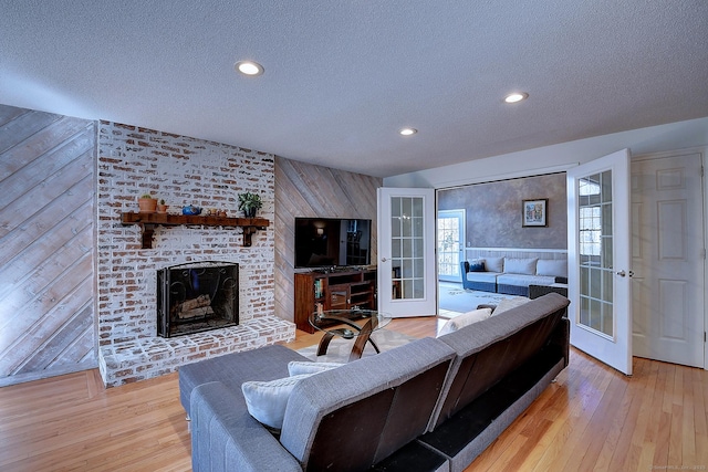 living room featuring french doors, a fireplace, wood walls, and light wood finished floors