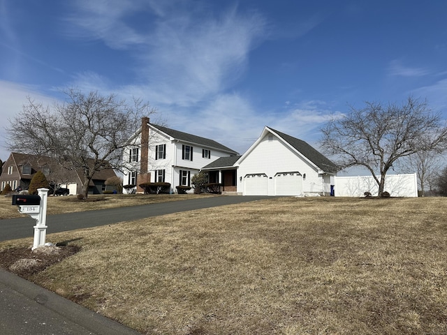 view of front of home with a front lawn, a chimney, an attached garage, and aphalt driveway