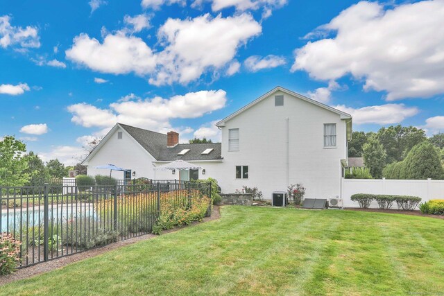 rear view of house with central air condition unit, fence, and a lawn