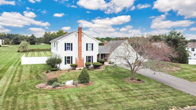 view of front of home featuring driveway, a chimney, a front lawn, and fence