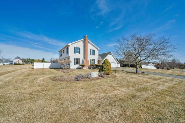 view of side of home with a yard, fence, driveway, and a chimney