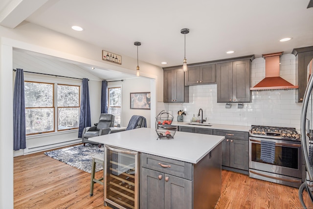 kitchen with stainless steel gas stove, beverage cooler, baseboard heating, wall chimney range hood, and a sink