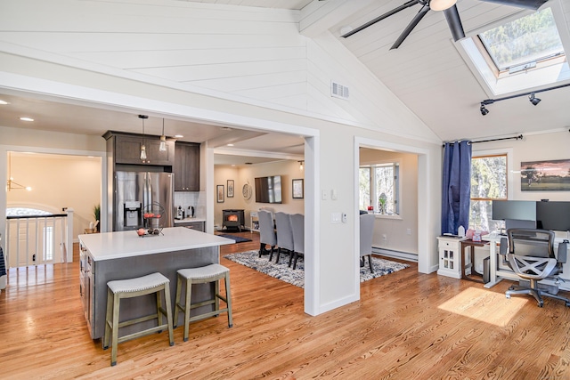 kitchen featuring light wood-style floors, vaulted ceiling with skylight, stainless steel refrigerator with ice dispenser, and light countertops