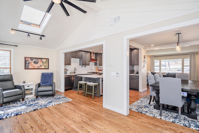 living area featuring a healthy amount of sunlight, light wood-style flooring, vaulted ceiling with skylight, and visible vents