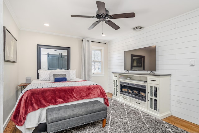 bedroom featuring wood finished floors, visible vents, baseboards, a glass covered fireplace, and crown molding