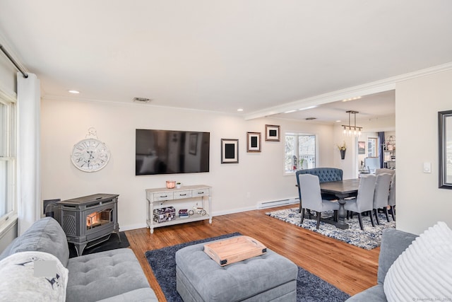 living room featuring a baseboard heating unit, ornamental molding, wood finished floors, and a wood stove