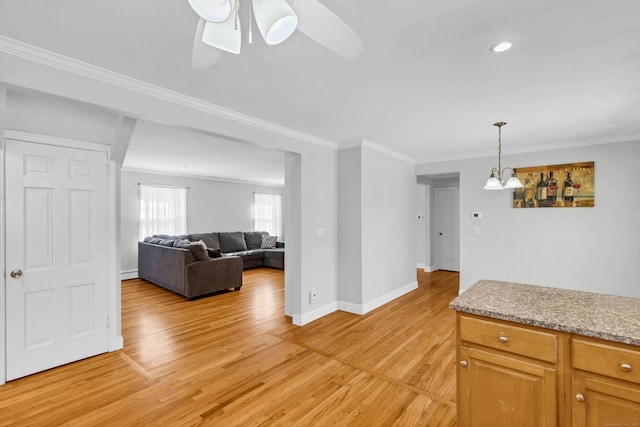 interior space with light wood-style flooring, a ceiling fan, baseboards, ornamental molding, and pendant lighting