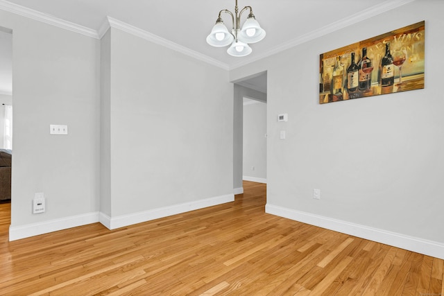 empty room featuring a notable chandelier, light wood-style floors, baseboards, and crown molding