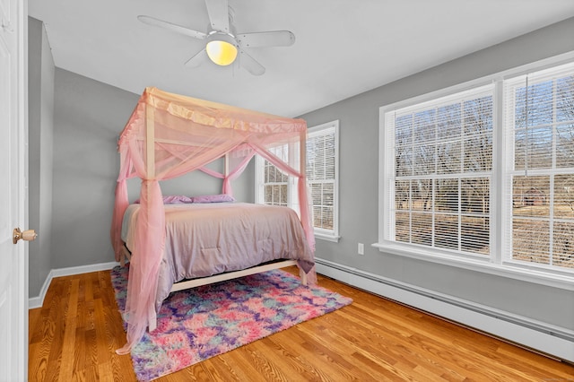 bedroom featuring baseboard heating, wood finished floors, a ceiling fan, and baseboards