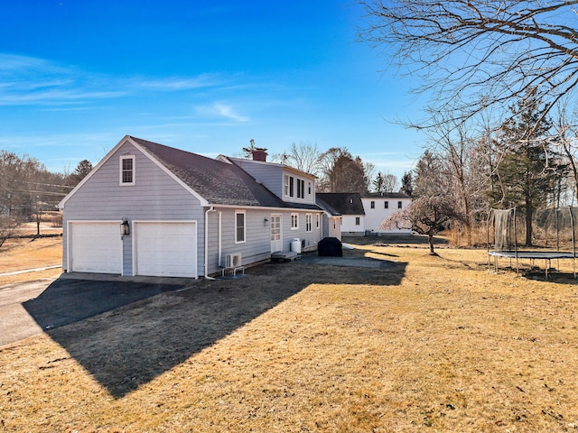 view of property exterior featuring a garage, driveway, a shingled roof, a chimney, and a trampoline