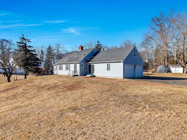 view of front of home with a detached garage, a chimney, and a front yard