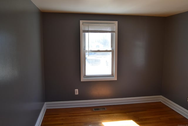 spare room featuring wood finished floors, visible vents, and baseboards