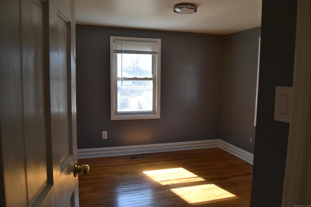 spare room with visible vents, baseboards, and dark wood-type flooring