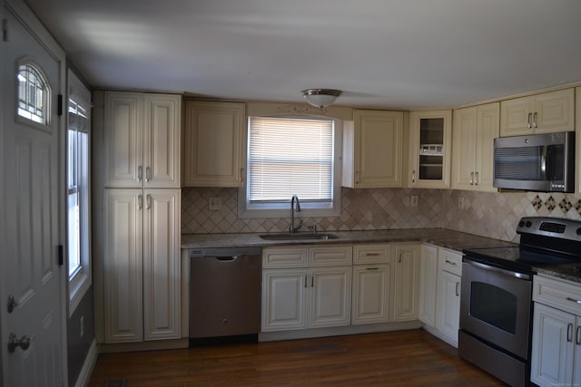 kitchen with dark wood-style floors, appliances with stainless steel finishes, a sink, and glass insert cabinets