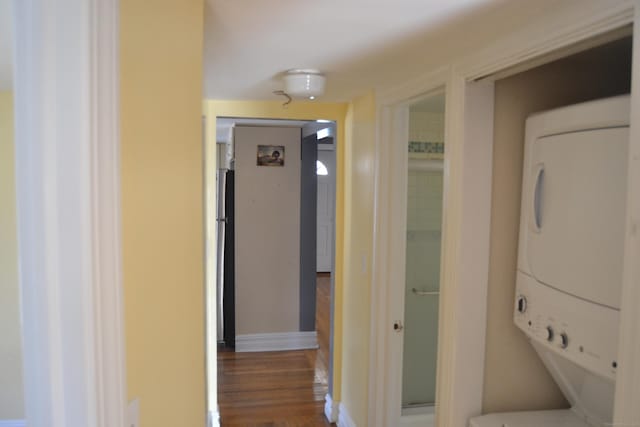 corridor featuring baseboards, stacked washer / drying machine, and wood finished floors