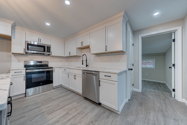 kitchen featuring light wood-style flooring, light stone countertops, stainless steel appliances, a sink, and decorative backsplash