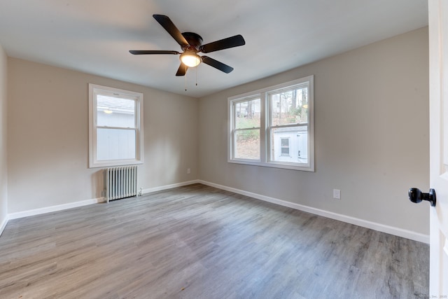 empty room featuring baseboards, ceiling fan, wood finished floors, and radiator