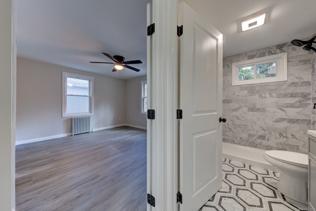 bathroom featuring toilet, a ceiling fan, baseboards, a tile shower, and radiator heating unit