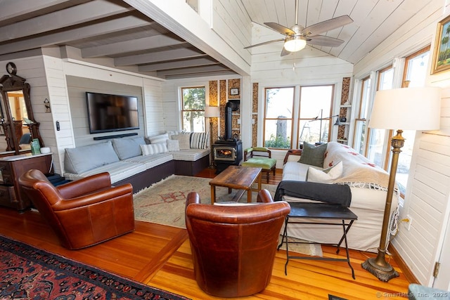 living area featuring wooden walls, wood finished floors, a wood stove, ceiling fan, and vaulted ceiling