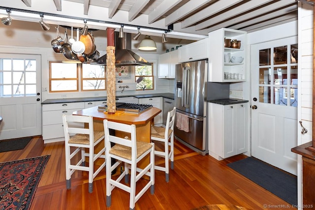 kitchen with dark wood finished floors, white cabinets, appliances with stainless steel finishes, dark countertops, and wall chimney range hood