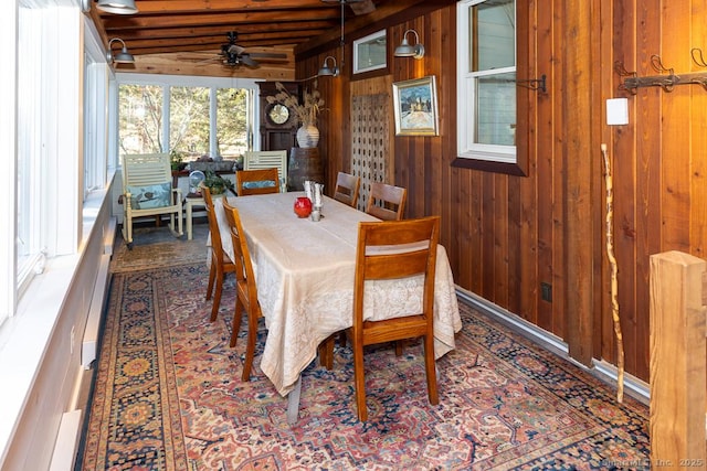 dining space featuring ceiling fan, beamed ceiling, wood walls, and a sunroom