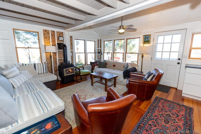 living room featuring lofted ceiling with beams, a wood stove, wood finished floors, and ceiling fan