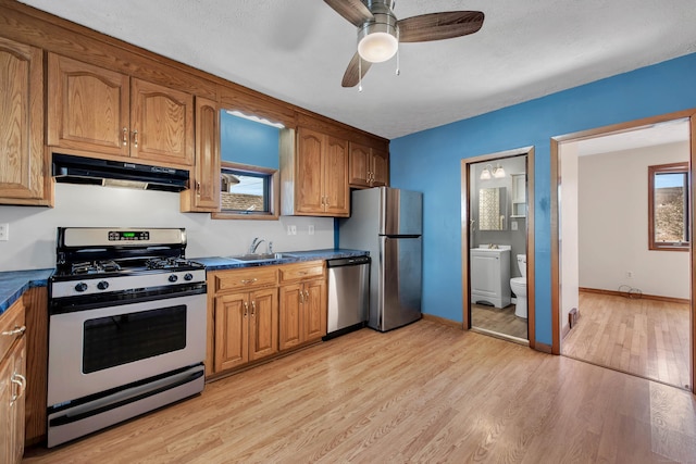 kitchen featuring appliances with stainless steel finishes, dark countertops, a sink, and under cabinet range hood