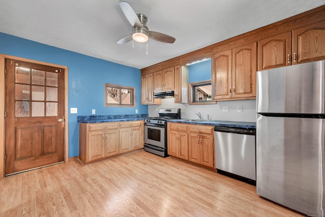 kitchen featuring stainless steel appliances, dark countertops, under cabinet range hood, and light wood finished floors