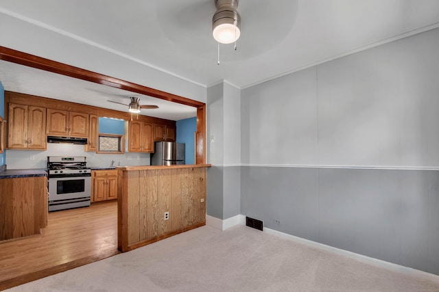 kitchen featuring stainless steel appliances, ornamental molding, a ceiling fan, light carpet, and under cabinet range hood