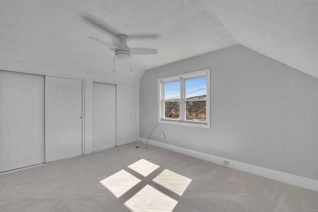 unfurnished bedroom with lofted ceiling, ceiling fan, carpet flooring, and two closets