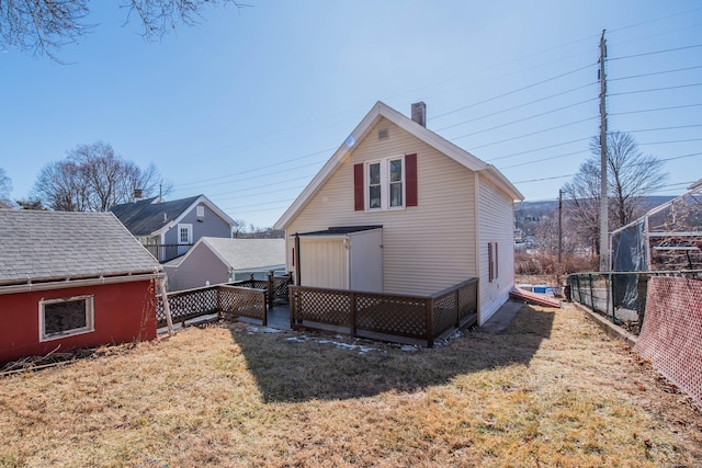 back of property with fence, a chimney, an outdoor structure, and a lawn