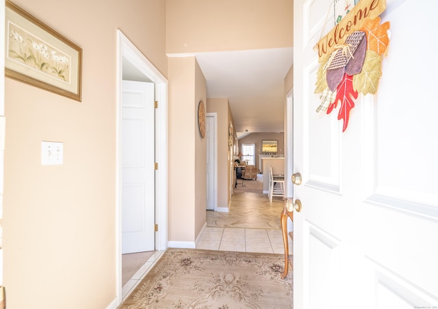 corridor featuring lofted ceiling, light tile patterned floors, and baseboards