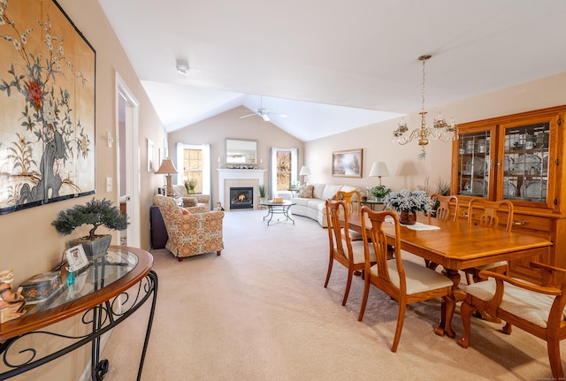 dining space featuring light carpet, ceiling fan with notable chandelier, a glass covered fireplace, and lofted ceiling