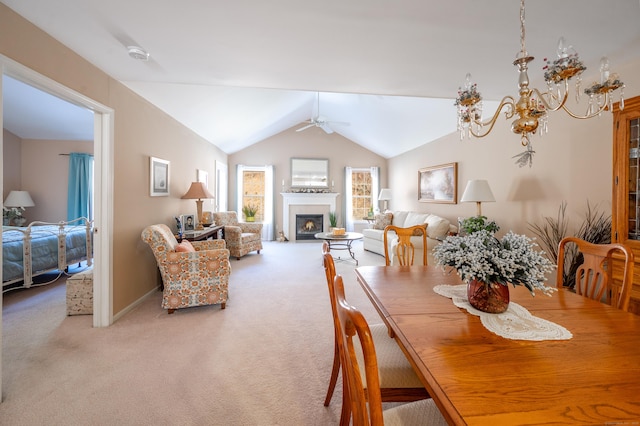 dining space with carpet flooring, vaulted ceiling, a tiled fireplace, and ceiling fan with notable chandelier