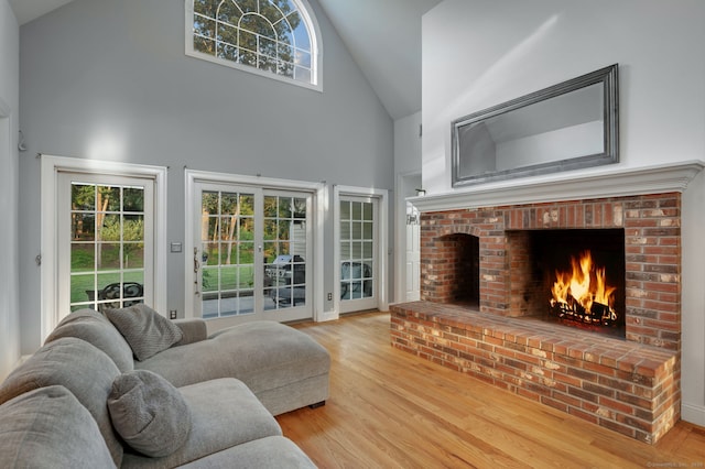 living room with high vaulted ceiling, a brick fireplace, and wood finished floors