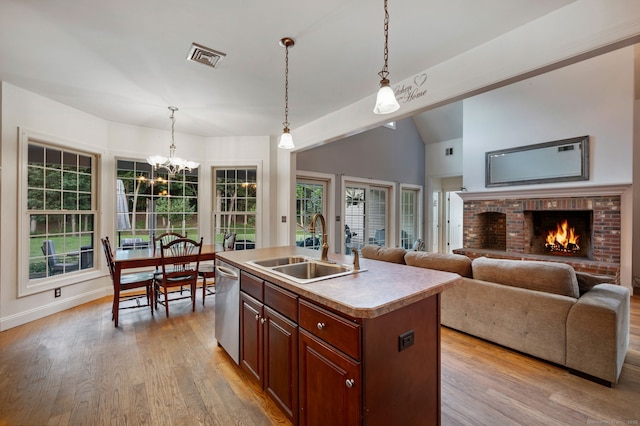 kitchen with hanging light fixtures, stainless steel dishwasher, a sink, and light wood-style floors