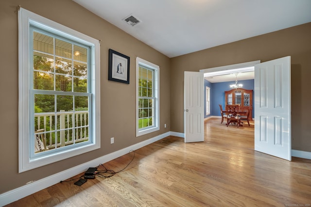 unfurnished room featuring light wood-type flooring, baseboards, visible vents, and a chandelier