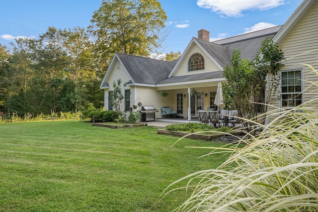 back of house featuring a shingled roof, a patio area, a lawn, and a chimney