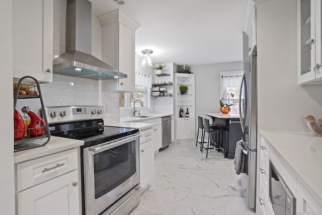 kitchen with marble finish floor, stainless steel appliances, tasteful backsplash, a sink, and wall chimney range hood