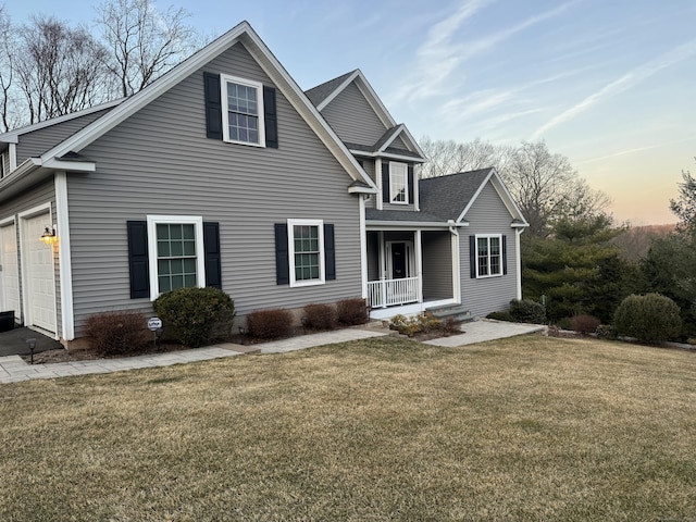 traditional-style home with a front yard, a garage, covered porch, and roof with shingles