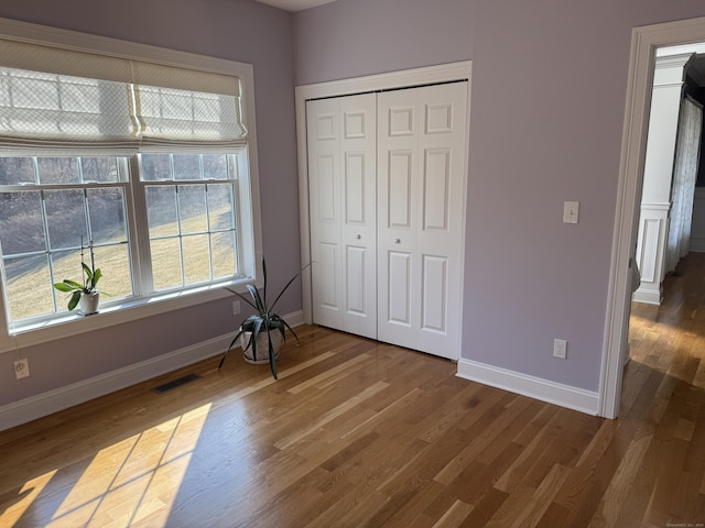 bedroom with wood finished floors, baseboards, visible vents, and a closet