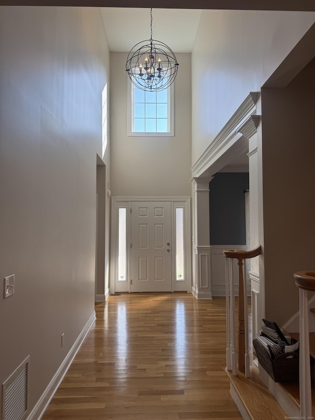 foyer with visible vents, baseboards, a towering ceiling, wood finished floors, and a notable chandelier