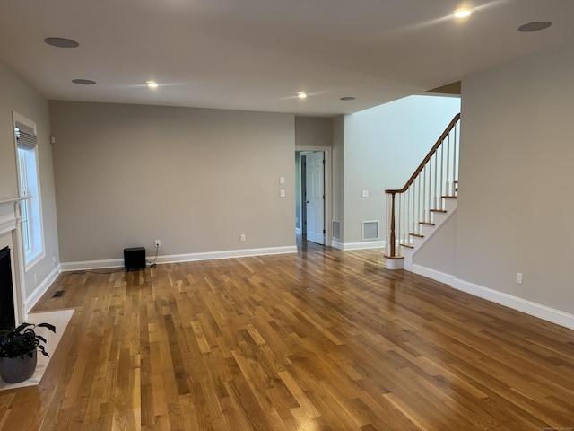 unfurnished living room featuring visible vents, a fireplace with flush hearth, wood finished floors, stairway, and baseboards